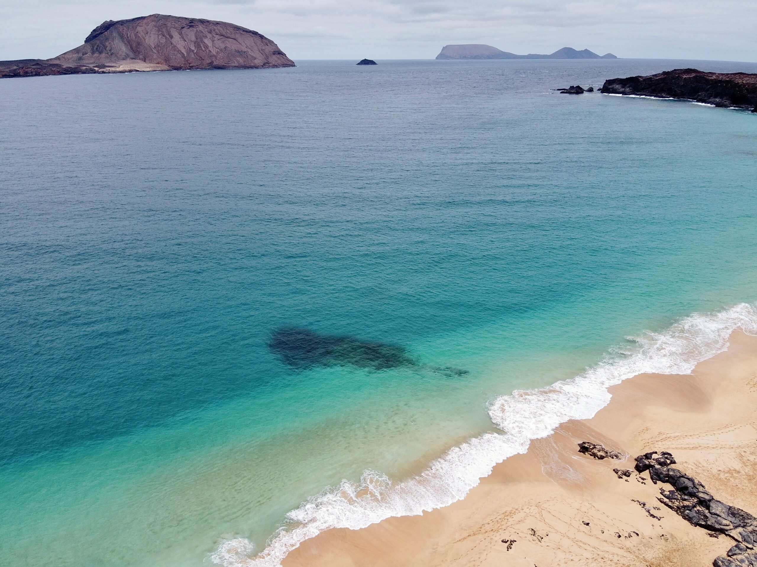 quelle-ile-des-canaries-choisir-orhantheworld-la-graciosa-plage-de-sable-brun-avec-les-vagues-de-locean-secrasant-sur-le-rivage-pendant-la-journee