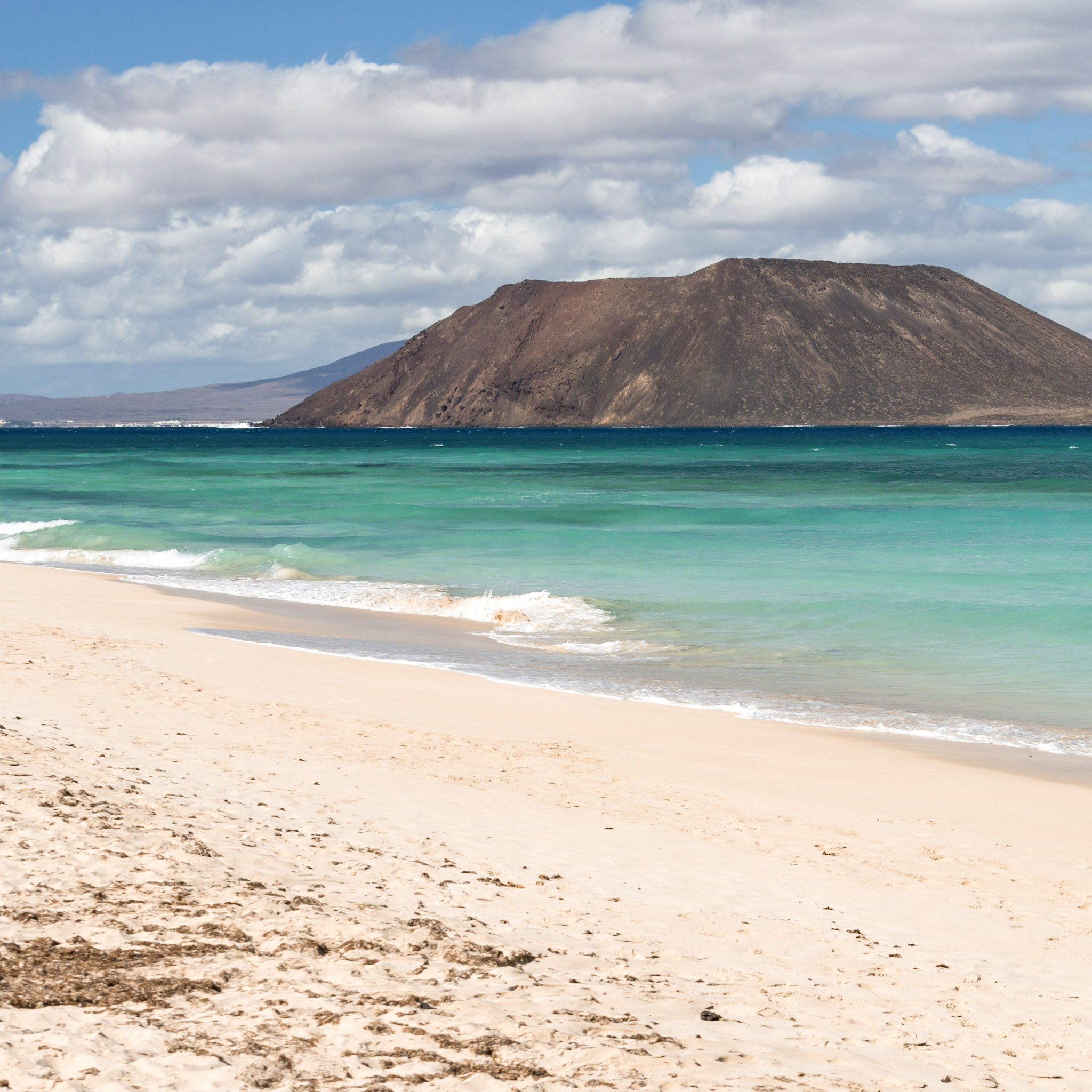 plage-de-sable-bordee-deau-turquoise-avec-un-volcan-en-arriere-plan